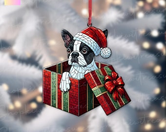 Könnte beinhalten: Weihnachtsbaumschmuck mit einem Boston Terrier Hund, der einen Weihnachtsmannhut trägt und aus einer rot-grünen Geschenkbox kommt. Der Schmuck ist im Glasmalerei-Effekt gestaltet und hat ein rotes Band zum Aufhängen.