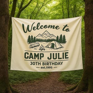 May include: A cream-colored banner with the text "Welcome to Camp Julie" in dark green. The banner features a mountain and forest graphic, a tent, and the text "30th Birthday - est.1995". The banner is hanging between two trees.