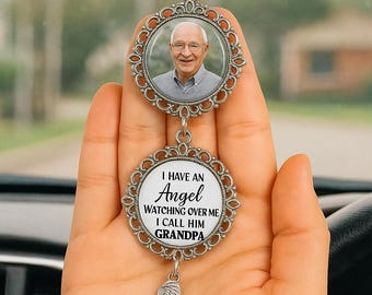 Könnte beinhalten: Ein silberner Autoanhänger mit zwei runden Anhängern. Der obere Anhänger zeigt ein Foto eines lächelnden Mannes. Der untere Anhänger lautet "I HAVE AN ANGEL WATCHING OVER ME I CALL HIM GRANDPA" mit einem baumelnden Flügel-Anhänger.