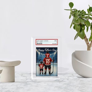 May include: A framed Father's Day print featuring a hockey-themed illustration. The image shows a father and child in hockey jerseys with the text "Happy Father's Day." The jerseys are red with the number 10. The frame includes text: "2025 Family League No. 1 Dad."