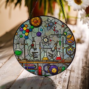 May include: A round stained glass window featuring a science lab theme. The design includes colorful molecules, beakers, microscopes, and other lab equipment. The window is framed with a dark metal and hangs from a chain.