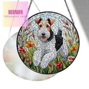 May include: A stained glass suncatcher featuring a wirehaired fox terrier dog in a field of flowers. The dog is white with black markings and is surrounded by green grass and colorful flowers.