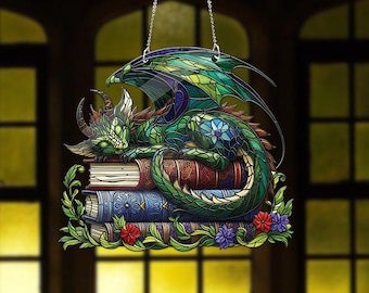 Peut inclure: Une décoration suspendue en vitrail représentant un dragon vert enroulé sur une pile de livres. Le dragon a des écailles bleues et vertes et une longue queue. Les livres sont décorés de motifs complexes et ont une bordure florale.