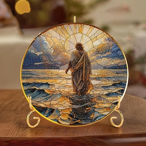 May include: A round stained glass art piece depicting a figure walking on water, with a golden frame and stand. The artwork features a sunset, water, and sky in shades of blue, gold, and brown. The piece is displayed on a wooden surface.