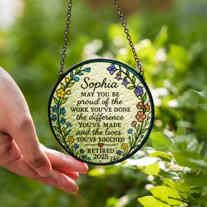 May include: A round, stained glass ornament with a floral border and the name "Sophia." The text reads "May you be proud of the work you've done, the difference you've made and the lives you've touched. Retired 2025."