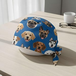 May include: A blue head covering featuring a repeating pattern of various dog breeds. The dogs are depicted with their faces, showcasing different colors and markings. The head covering is likely made of fabric and has a tied closure.