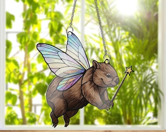 Op de afbeelding: Een hangende ornament van gekleurd glas met een bruine wombat met iriserende blauwe en paarse vleugels en een gouden stervormige toverstaf.
