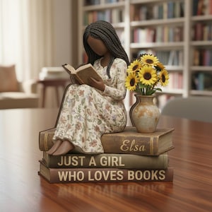 Könnte beinhalten: Dekorative Figur einer lesenden Person, die auf einem Bücherstapel sitzt. Die Bücher tragen die Aufschriften "Just a Girl Who Loves Books" und "Elsa". Eine Vase mit Sonnenblumen steht neben der Figur. Die Person trägt ein Blumenkleid.