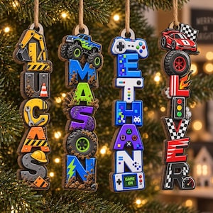 May include: Four vertical wooden ornaments hanging by twine, each featuring a name spelled out with themed graphics: LUCAS with construction icons, MASON with monster trucks, ETHAN with video game controllers, and OLIVER with race car motifs.