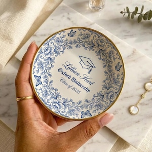 May include: A set of three ceramic mugs with a speckled, cream-colored glaze. Each mug features a different hand-painted design: a blue and green leaf, a yellow flower, and a red berry. The mugs have a simple, rounded shape.