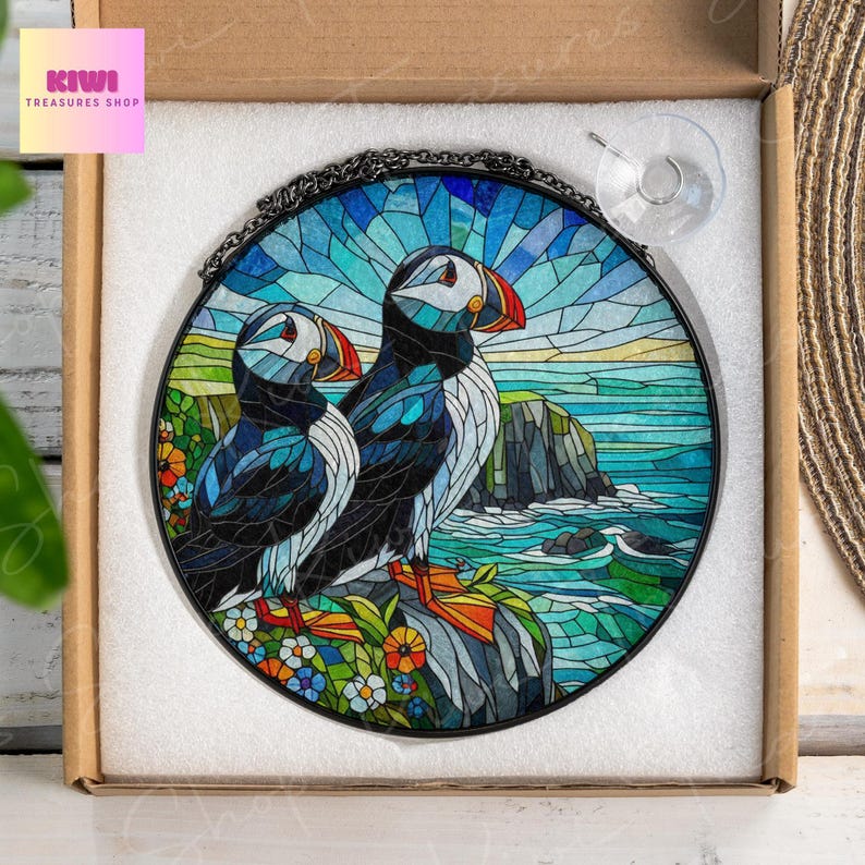 Puede incluir: Una ventana de vidrio emplomado colgante representa dos frailecillos posados en una roca, con un oc&eacute;ano azul y un acantilado en el fondo. Los frailecillos son negros y blancos con picos naranjas.