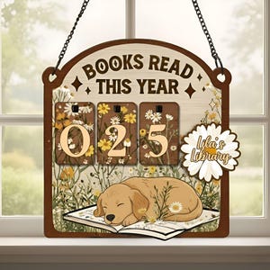 May include: Wooden sign with the text "BOOKS READ THIS YEAR" and the number "025" displayed on a floral background. A sleeping golden retriever rests on an open book. The sign also features the text "Lila's Library".