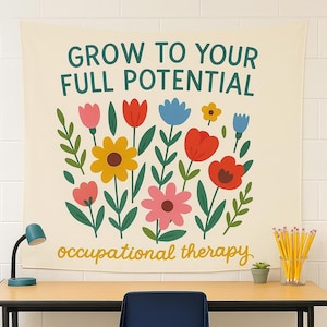 May include: A cream-colored wall tapestry with the text "GROW TO YOUR FULL POTENTIAL" and "occupational therapy". The tapestry features a colorful floral design with pink, yellow, red, and blue flowers and green leaves. A desk with a lamp, pencils, and a small plant is in front of the tapestry.