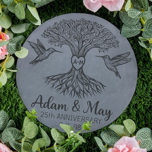 Może przedstawiać: Szary kamień ogrodowy z motywem drzewa życia, dwoma kolibrami i napisem "Adam & May 25th Anniversary". Drzewo ma serce z "A-M". Otoczony zielenią i różowymi kwiatami.