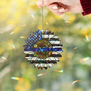 May include: A blue and white sunflower ornament with a thin blue stripe across the center. The ornament is hanging from a silver chain.