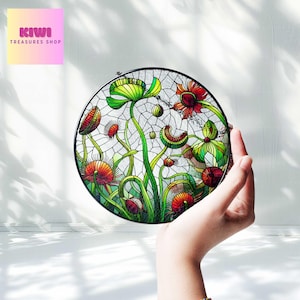 May include: A round stained glass window with a floral design. The design features green leaves, red and orange flowers, and a black metal frame.