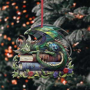 May include: A decorative dragon ornament with a stained-glass effect. The green dragon is curled up on a stack of books, with red, blue, and gold covers. The ornament is trimmed with flowers and greenery and has a red ribbon for hanging.