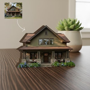Puede incluir: Una maqueta en miniatura de una casa de dos plantas con revestimiento de tejas verde oliva, tejado a dos aguas marrón y cimientos de piedra. El porche delantero incluye una puerta de madera, ventanas y flores azules en la base.