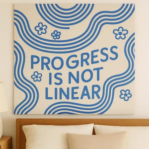 May include: A square canvas art piece with the text "PROGRESS IS NOT LINEAR" in blue. The artwork features blue wavy lines and flower shapes on a cream background. The canvas is mounted above a bed.