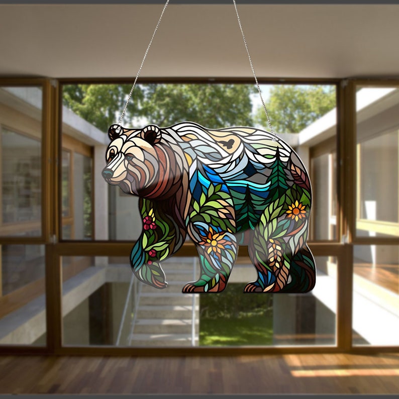 Puede incluir: Una silueta de oso de estilo vitral con un dise&ntilde;o colorido de monta&ntilde;as, &aacute;rboles y flores. El oso est&aacute; colgado de una cadena plateada.