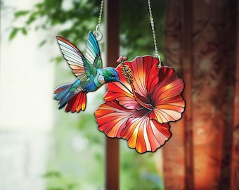 May include: A stained glass hummingbird with blue, green and red wings is perched on a red hibiscus flower. The hummingbird and flower are hanging from a silver chain.