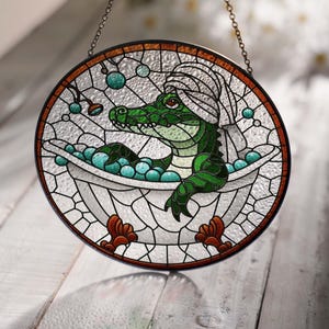 May include: A stained glass window hanging with a green alligator wearing a white towel on its head, relaxing in a white bathtub with blue bubbles.