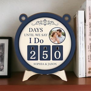 May include: A navy blue and cream wedding countdown clock displaying "DAYS UNTIL WE SAY I DO" and the number "250". Features a photo of a couple and the names "SOPHIA & JASON".