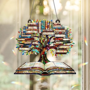 May include: Stained glass window art depicting a tree made of books. The tree trunk and branches are brown, with colorful leaves. The books are stacked to form the tree's canopy. An open book forms the base of the tree, with a chain for hanging.