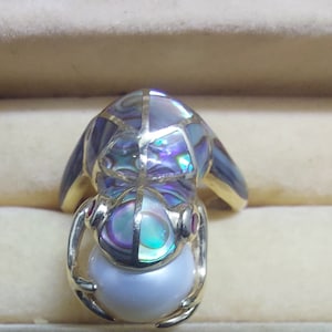 May include: A gold ring with a frog design. The frog is made of iridescent abalone shell and has a pearl in its mouth.