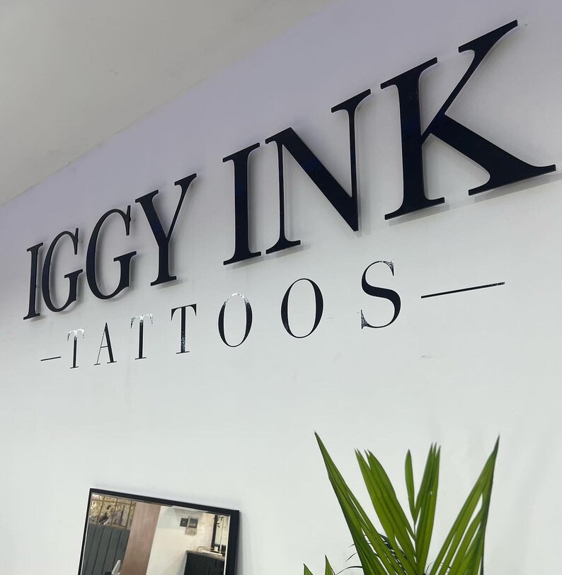 May include: Black and white sign with the text "IGGY INK - TATTOOS" on a white wall.