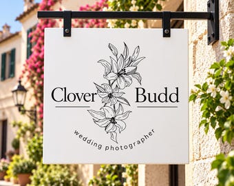 May include: A square white hanging sign with a black metal bracket. The sign features a black line drawing of lilies in the center, with the text Clover Budd and the words wedding photographer printed in a black serif and sans-serif font.