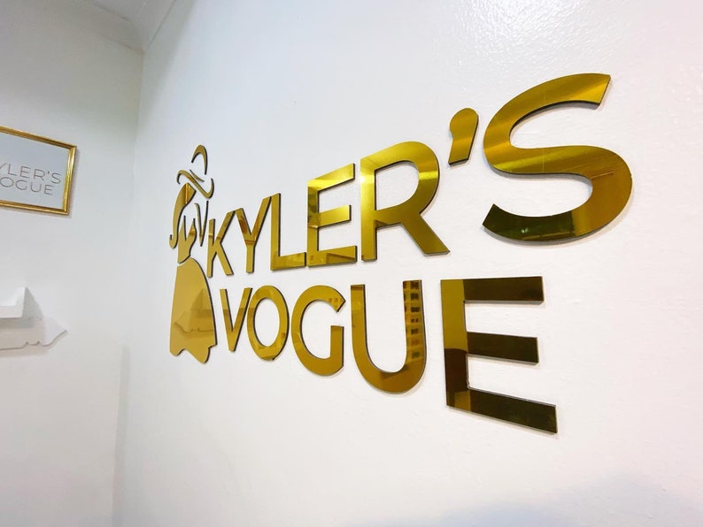 May include: Gold-colored sign with the text "KYLER'S VOGUE" and a stylized female figure wearing a hat and dress.