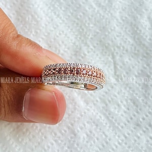 May include: A silver band ring with three rows of diamonds. The center row features brown diamonds, while the top and bottom rows feature white diamonds.