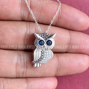 Puede incluir: Un collar de plata con un colgante de búho con piedras de circonita cúbica transparentes y azules. El búho tiene un diseño detallado con una cadena de plata.