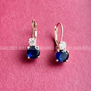 Könnte beinhalten: Ein Paar goldene Creolen mit einem blauen und weißen Edelstein. Die Ohrringe haben ein schlichtes Design und sind perfekt für den Alltag.