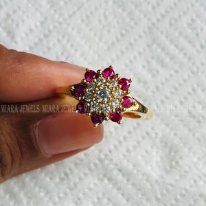 Pode incluir: Um anel de ouro com um design de flor vermelha e branca. A flor tem um centro de pequenas pedras brancas cercadas por pedras vermelhas maiores.