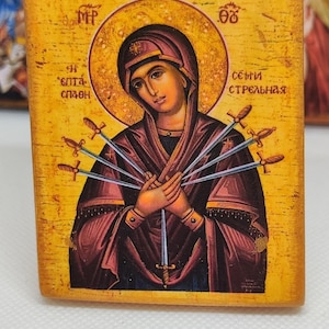 Peut inclure: Icône religieuse en bois représentant une femme auréolée, percée d'épées. L'icône présente des tons or et bordeaux, avec du texte en cyrillique. Le fond est d'un jaune chaud et vieilli.