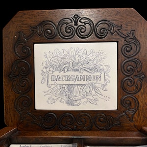 Puede incluir: Un juego de backgammon de madera con un diseño floral y la palabra "BACKGAMMON" en una baldosa blanca. El juego tiene un marco marrón oscuro con tallas ornamentadas e incluye piezas de juego.