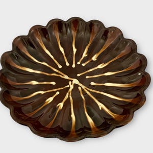 Op de afbeelding: Een bruine en gouden keramische serveerschaal met een gegolfde rand en een zonnestralenontwerp.
