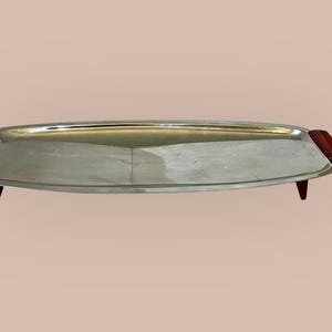 May include: A silver serving tray with red wooden handles and four legs. The tray is oval shaped and has a polished finish.