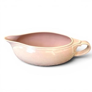 Peut inclure: Un saucier en céramique rose pâle avec une anse et un bec verseur. Le bateau a une forme arrondie avec un bord décoratif et une finition lisse et brillante. L'intérieur est d'une nuance de rose légèrement plus foncée.