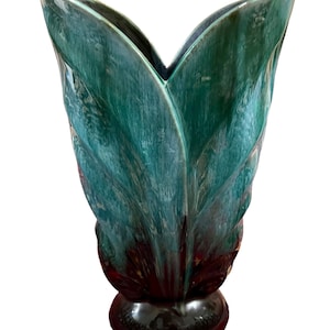 May include: A teal ceramic vase with a distinctive leaf design. The vase has a glossy finish and a dark brown base. The vase's shape resembles a flower, making it a decorative piece for the home. The vase is approximately 25 cm tall.