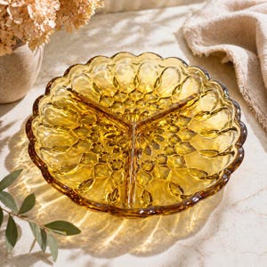 Könnte beinhalten: Bernsteinfarbene Servierschale mit drei Fächern und gewelltem Rand. Die Glasschale hat ein detailliertes, strukturiertes Muster und ist zum Servieren von Vorspeisen oder Snacks konzipiert. Die Schale ist rund und hat eine Vintage-Ästhetik.