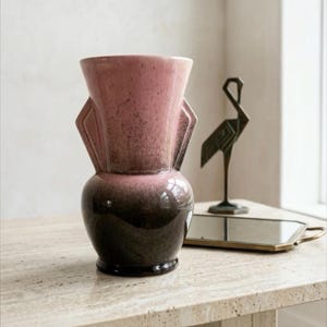 Peut inclure: Un vase en céramique avec un glaçage ombré bicolore passant d'un rose moucheté doux au niveau du col évasé à un brun foncé profond sur la base arrondie. Le vase présente deux anses latérales angulaires proéminentes sur le col.