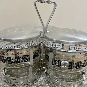 Peut inclure: Un ensemble de quatre bocaux en verre avec des couvercles argentés et une poignée argentée. Les bocaux ont un motif géométrique noir et blanc avec des accents dorés.