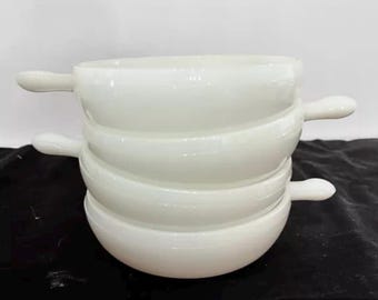 May include: Four white ceramic bowls with handles stacked on top of each other. The bowls are all the same size and shape.