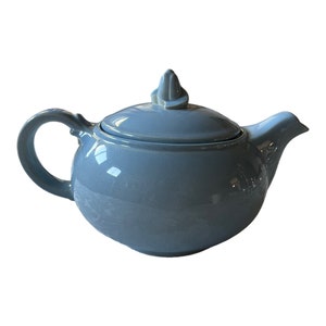 May include: A light blue ceramic teapot with a rounded body and a small, pointed lid. The teapot has a handle and a spout.