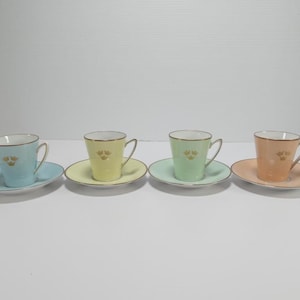May include: Set of four pastel-coloured teacups and saucers with gold trim and a gold floral design. The cups are light blue, yellow, green, and peach.