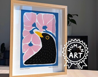 May include: A framed art print featuring a black bird with a yellow beak positioned against a blue background with stylized pink flowers. The text "Harbinger of Spring NO.3" and "SPRING COLLECTION 2023" is printed at the bottom of the white border.