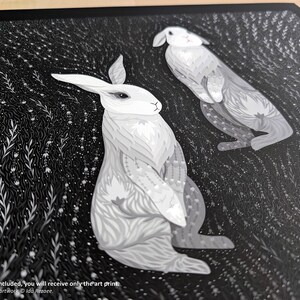 May include: An art print featuring two white rabbits with intricate grey patterns on their fur, set against a dark black background filled with detailed white botanical illustrations. The text at the bottom reads: NO frame is included, you will receive only the art print. Photograph and artwork &copy; Ida Rezaee.